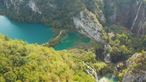 岩の多い崖と鬱蒼とした森の間の滝につながる明るいターコイズ ブルーの湖の信じられないほどの空撮ドローン ビュー