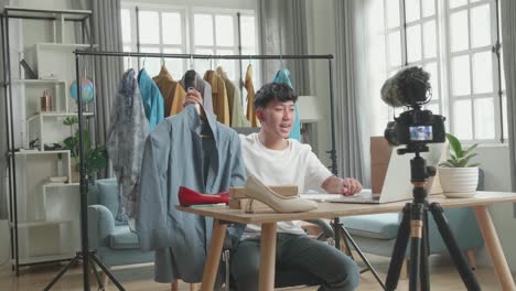 joven asiático lee comentarios en computadora y graba video con cámara para vender ropa en línea en casa