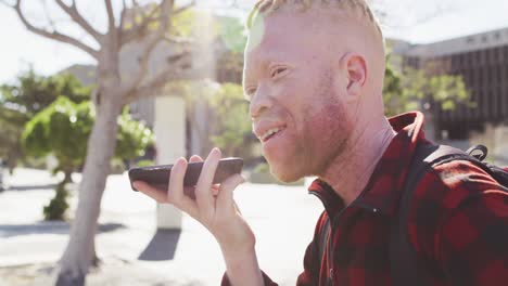 gelukkige albino afrikaanse amerikaanse man met dreadlocks in het park praten op een smartphone