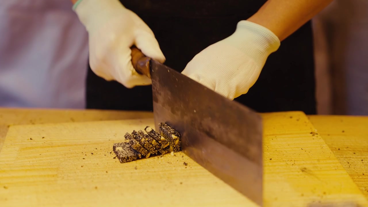 Artigiano che taglia il tradizionale dolce cinese al sesamo con un grande coltello