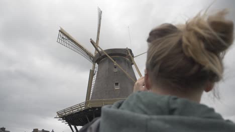 slow motion panning footage behind a woman taking a picture of an old windmill in the dutch countryside