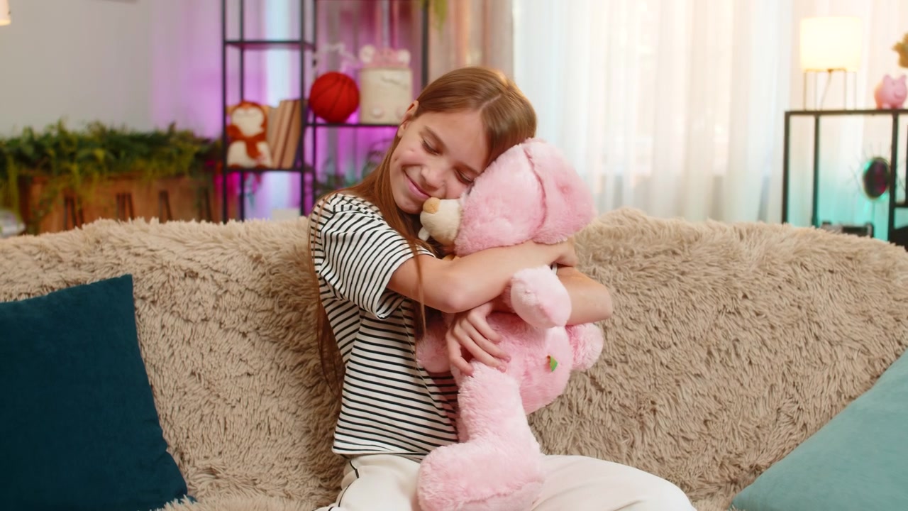 Glad barn pige barn krammer yndlings kaninlegetøj forsigtigt med smil, mens du sidder på en hyggelig sofa derhjemme