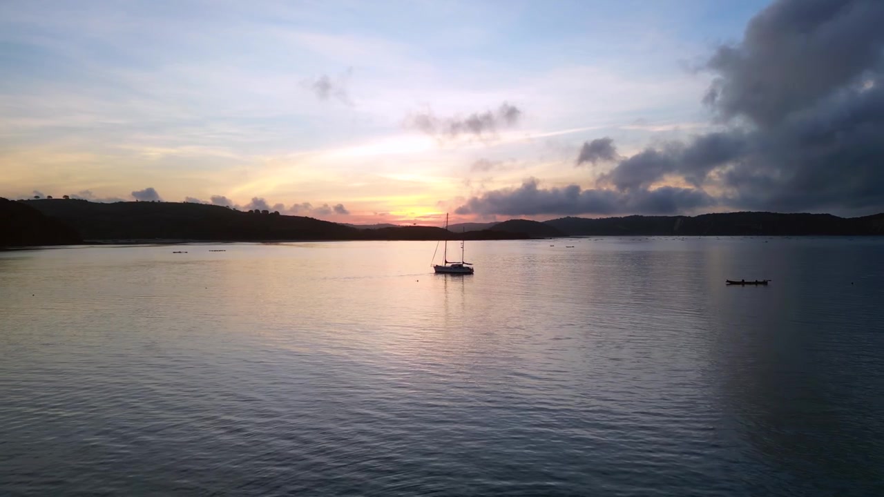 Costa del villaggio di Gerupuk all'alba con una barca a vela da pesca ormeggiata nella baia tranquilla, che riflette la calda luce del mattino. Fantastica vista aerea panoramica con drone che avanza