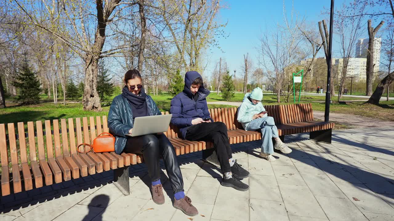 Family Using Digital Devices on a Park Bench on a Sunny Day