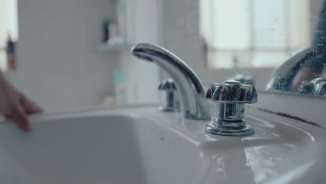 man turning on faucet and washing face above bathroom sink