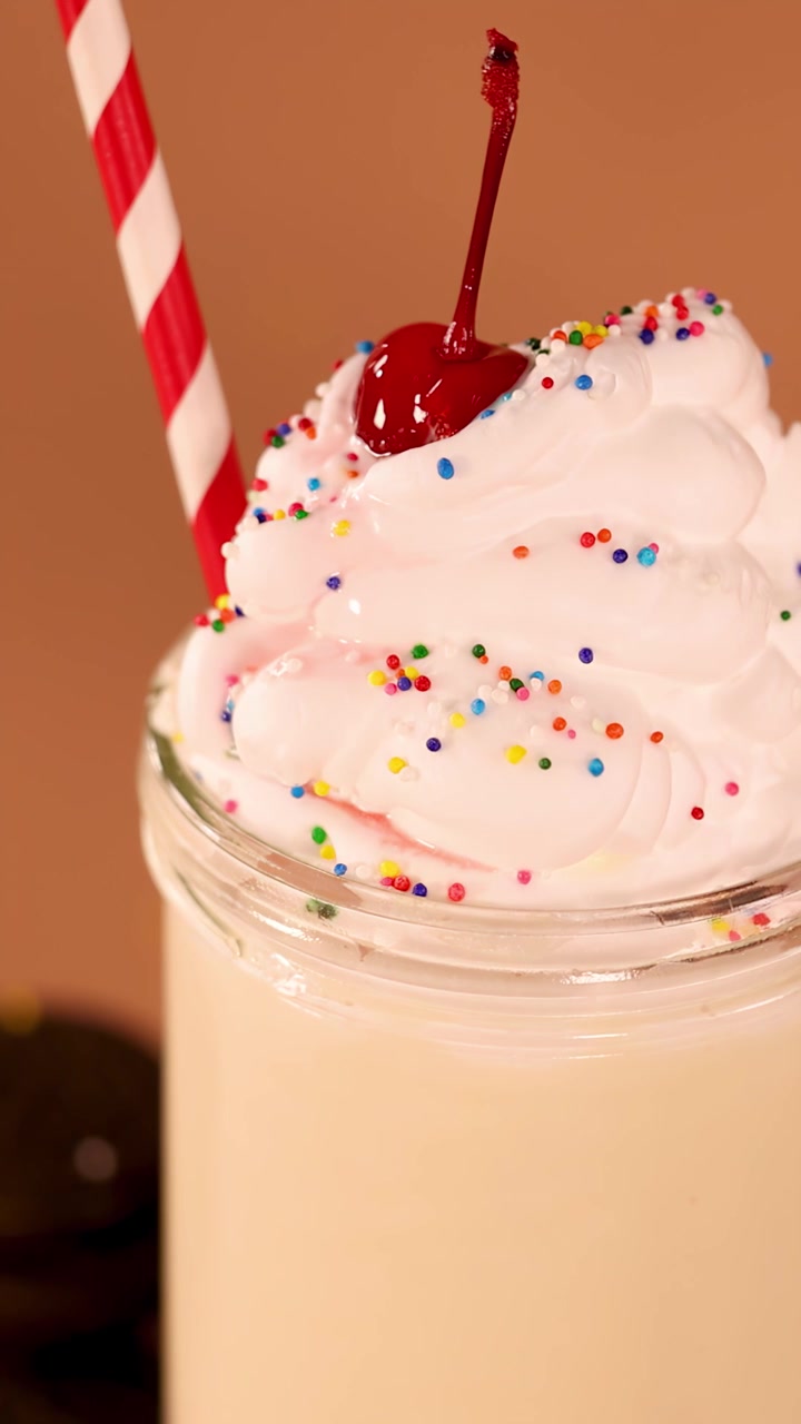 Milkshake alla vaniglia con panna montata e ciliegia in un barattolo di vetro