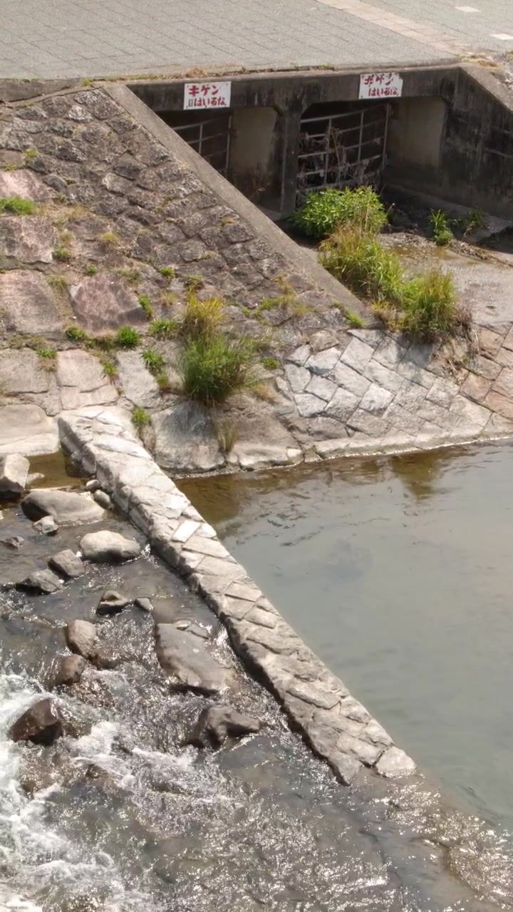 Toma estática en picado de agua fluyendo desde una alcantarilla de hormigón hacia una orilla de río revestida de piedra.