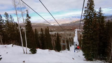 beautiful point of view from a ski lift at a ski resort in colorado on an overcast winter day with tall aspen and pine trees with stunning desert orange and red colored landscape in the background