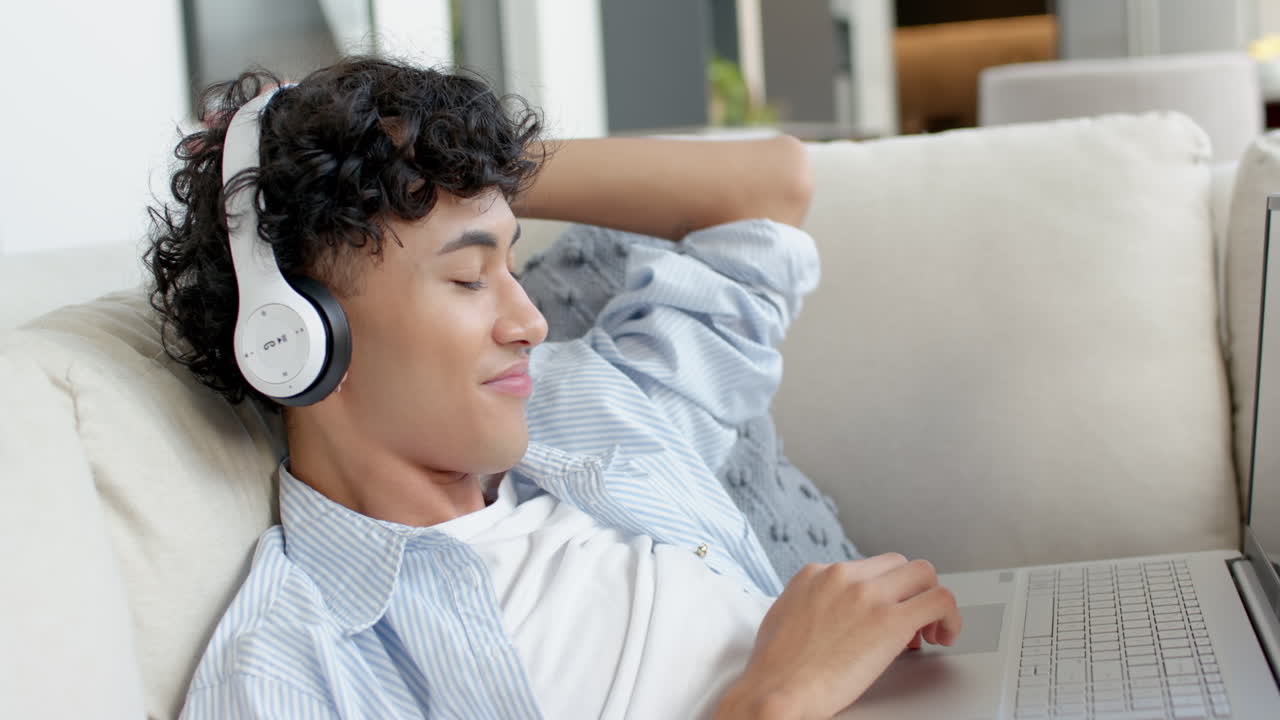 Relaxing on couch, teenage boy wearing headphones and using laptop at home