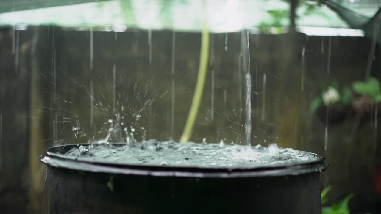 Heavy rain drops filling up rainwater harvesting barrel, closeup