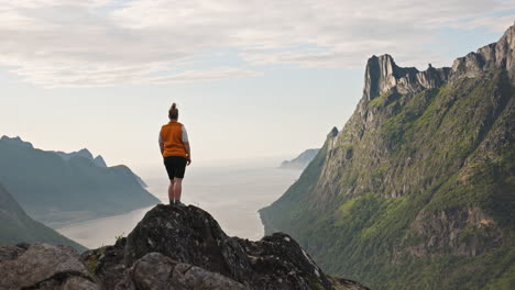 back of female hiker in front of jagged arctic mountain by senja norway fjord