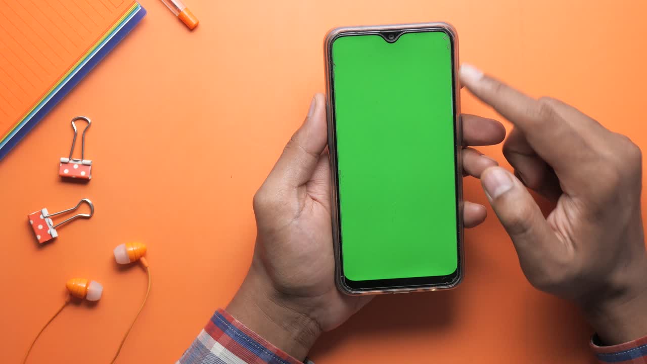 persona que utiliza un teléfono inteligente con una pantalla verde sobre un fondo naranja