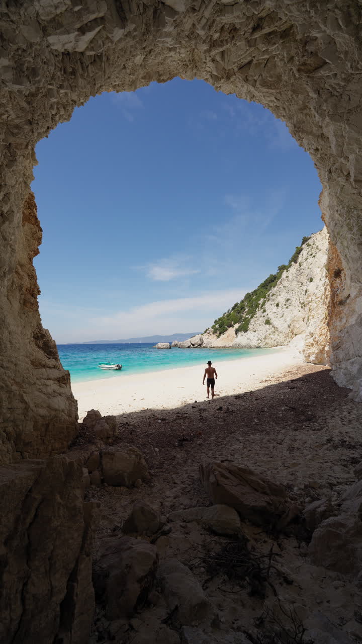 One man walks on the Platis ammos beach in Ithaca island, Greece. Static shot from inside the cave. Vertical