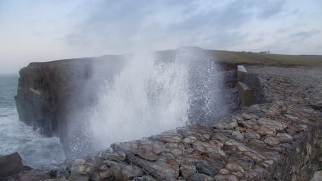 Big-Waves-Crashing-Through-Edge-Of-A-Cliff-In-Porth-Island-In-Newquay,-Cornwall,-UK---medium-shot