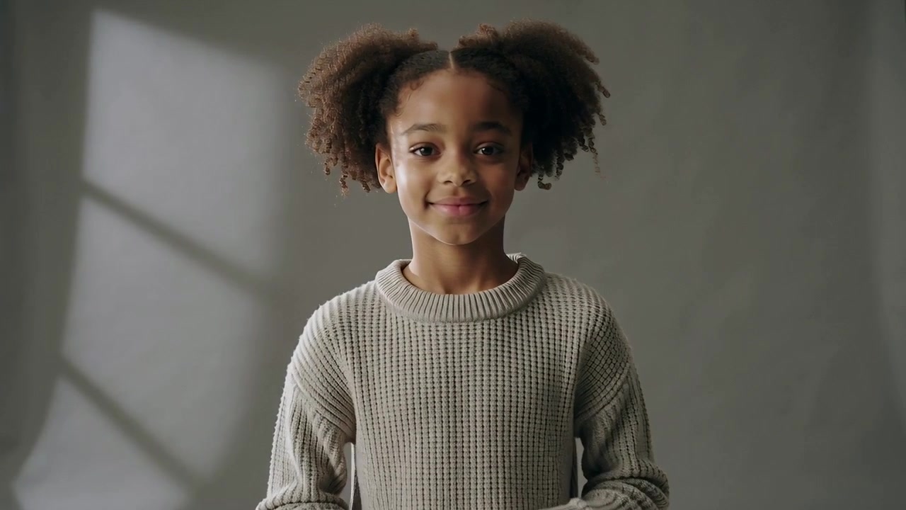Entering kid in knit sweater posing for portrait on gray backdrop with window shadow