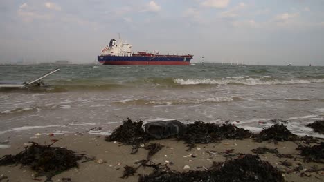 Ship-sailing-near-to-shore-with-rubbish-on-beach-on-foreground