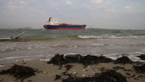 Schiff-Segelt-In-Küstennähe-Mit-Müll-Am-Strand-Im-Vordergrund