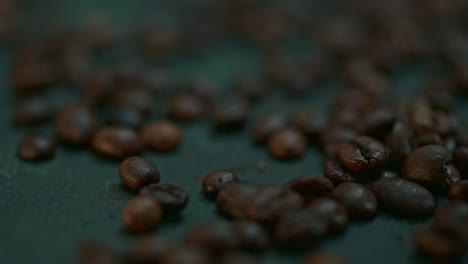 Close-up-coffee-beans-falling,-spilling-onto-the-dark-green-table