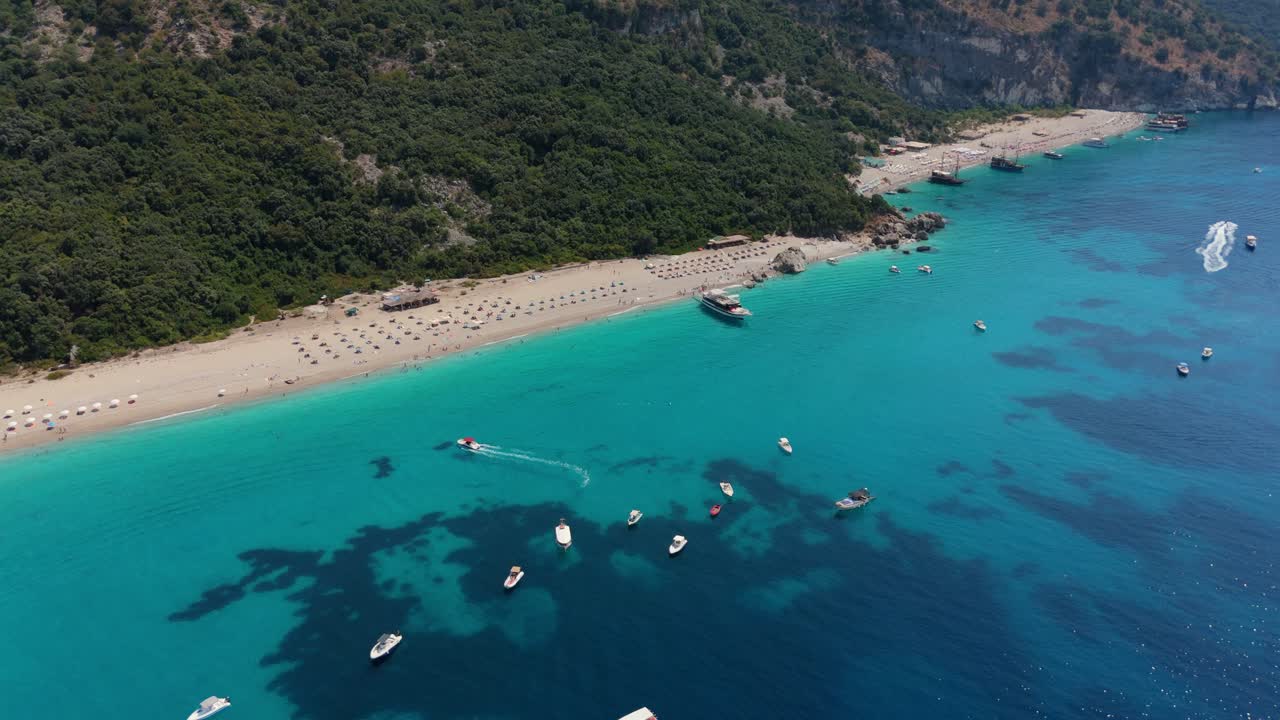 Boats anchored in crystal clear turquoise water by a sandy beach surrounded by lush greenery