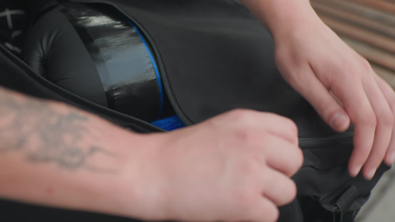 Preparando el equipo para el entrenamiento: persona concentrada organizando diligentemente los materiales de entrenamiento. Una persona con los brazos tatuados cierra cuidadosamente su bolsa de deporte llena de elementos esenciales para el entrenamiento.