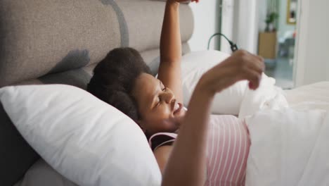 happy african american woman lying in bed, stretching in bedroom