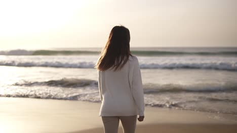 Brunette-woman-walks-alone-on-sandy-beach.-Girl-walking-on-sand-by-the-sea-or-ocean-in-casual-clothes-Beach-travel.-Summer-vacations-concepts.-Mild-dusk