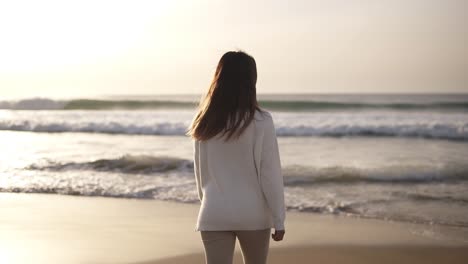 brunette woman walks alone on sandy beach. girl walking on sand by the sea or ocean in casual clothes beach travel. summer vacations concepts. mild dusk