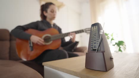 woman practicing guitar with metronome on table in living room