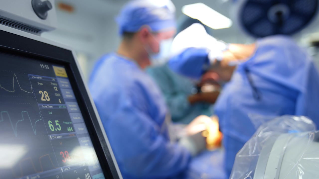 Patient's life parameters on the part of the monitor of lung ventilating machine. Medical team carries out surgery at backdrop in blur.