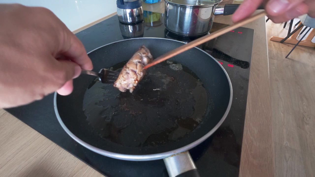 Juicy steak is seared in a nonstick frying pan, flipped with spatula and fork on a ceramic stovetop. Warm indoor lighting highlights rich texture and home cooking atmosphere.