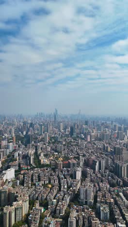 Vertical aerial view of Guangzhou’s cityscape during the day, featuring a vast skyline with modern skyscrapers, dense urban housing, and green spaces. China
