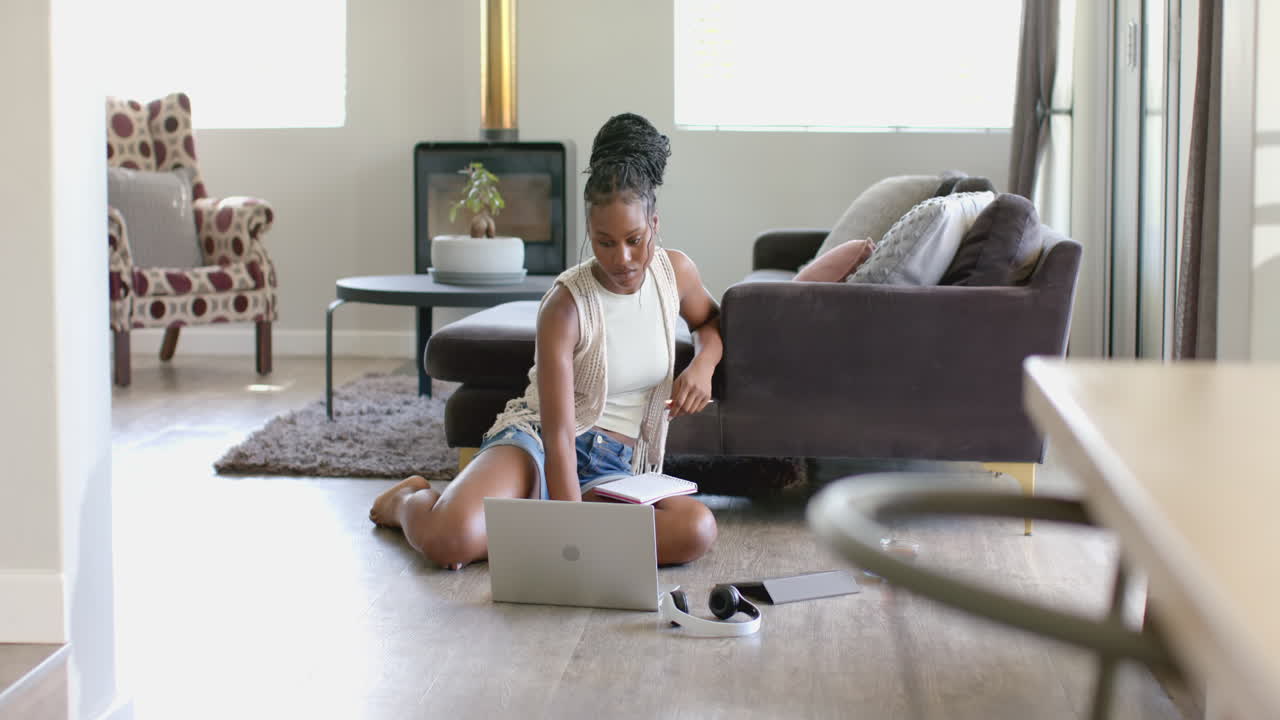 African American young woman sitting on floor, using laptop, at home