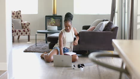 african american young woman sitting on floor, using laptop, at home