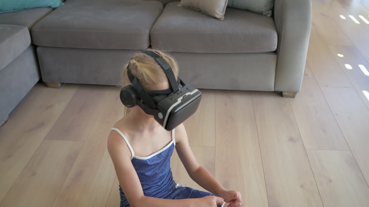 Niña con gafas de realidad virtual reaccionando a una señal, sentada en el suelo estirándose, girando y manipulando controles.