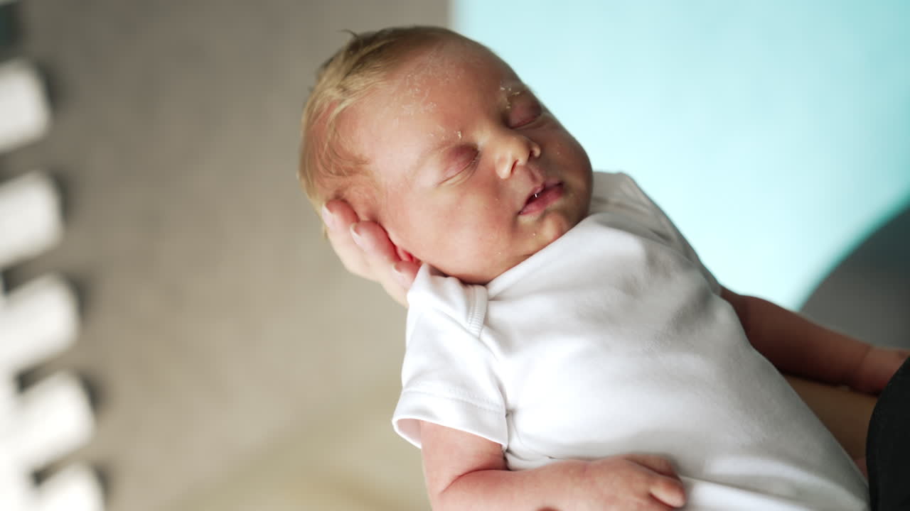 Little baby in white bodysuit peacefully sleeping on parent's hand. Father's finger is touching tiny kid's nose. Close up.