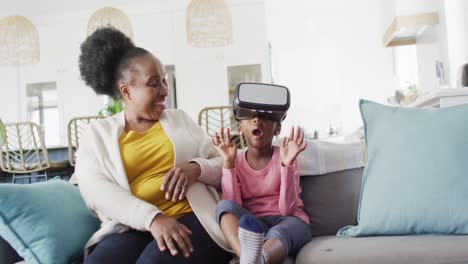 Excited-african-american-granddaughter-using-vr-headset-sitting-with-grandmother-at-home,-copy-space