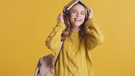 happy teenage caucasian girl student holding notebook on her head.