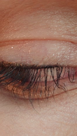 young woman opens eye with painted dark lashes and glitter shadow on eyelid. brown-eyed female person with professional makeup extreme closeup