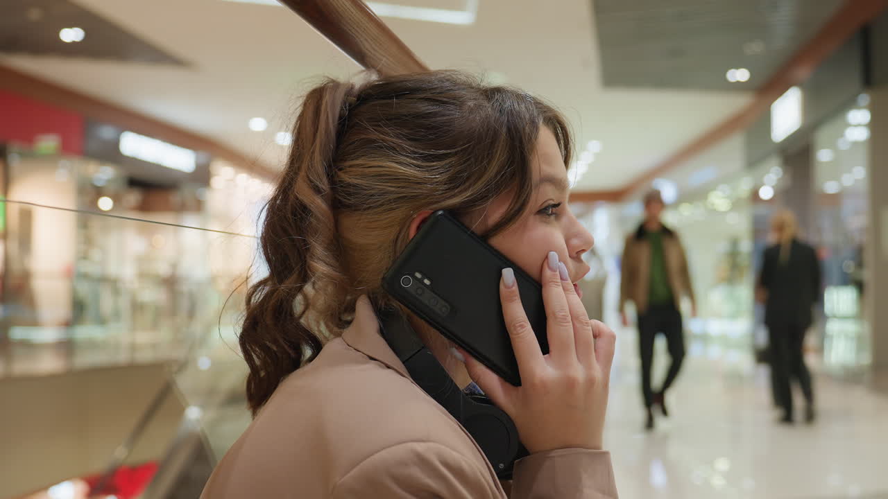 쇼핑몰을 걸어 다니며 채팅하는 여성, 번화한 쇼핑 센터를 걸어 다니며 소통하는 여성, 쇼핑객으로 가득 찬 활기 넘치는 몰 복도를 거닐면서 전화 통화하는 여성