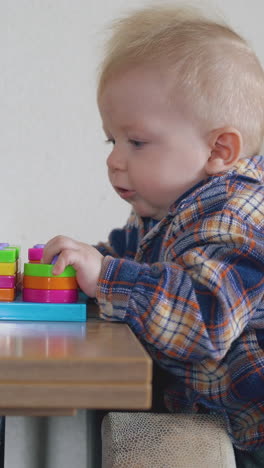 small blue eyed boy plays with bright colorful toy standing at low wooden table in light room close view