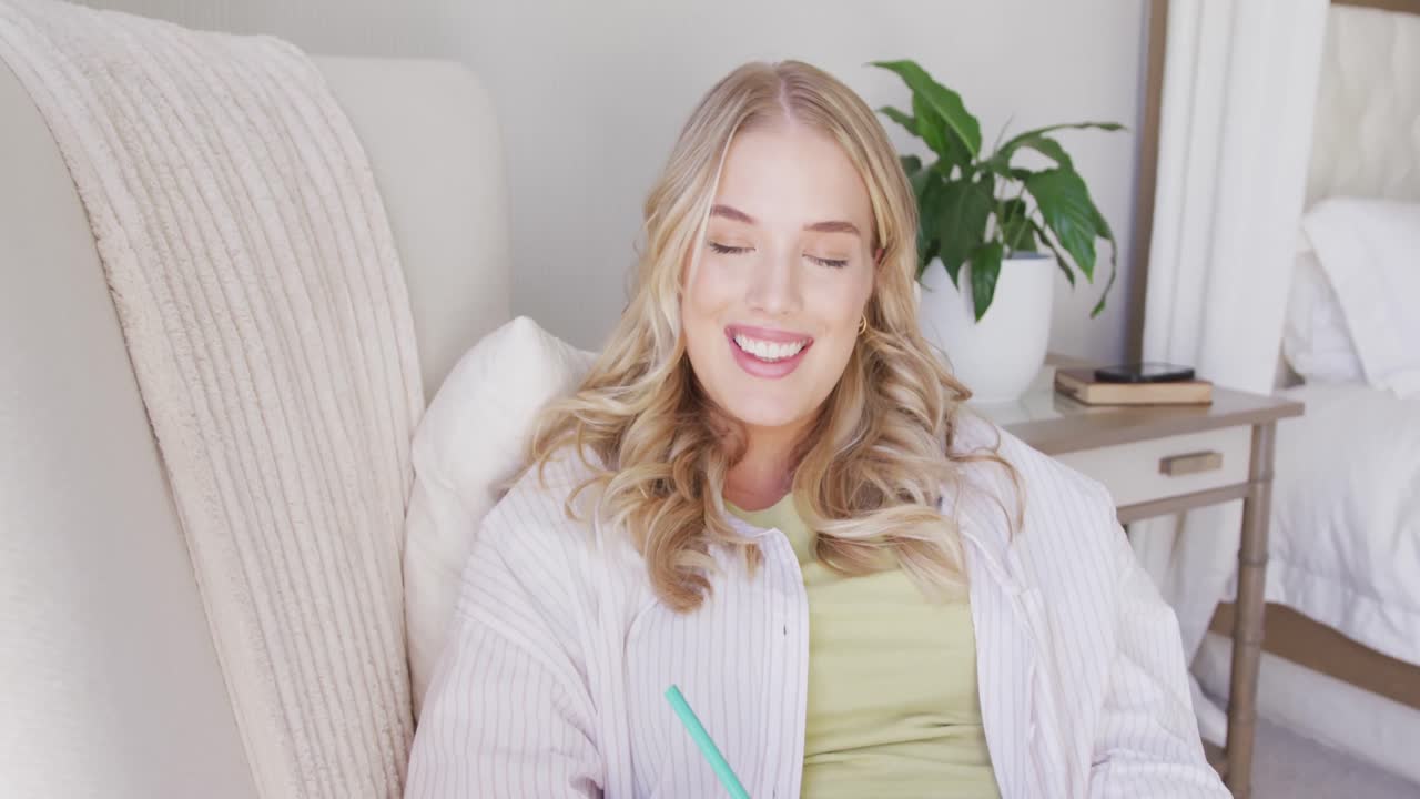 행복한 백인 플러스 사이즈 여성이 의자에 누워서 느린 동작으로 쓰고 있습니다.