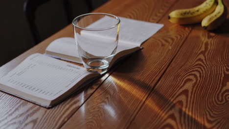 wooden table with notebook, glass, and bananas