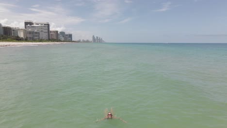 Aerial:-Young-Caucasian-woman-swimming-in-sunglasses-waves-at-camera