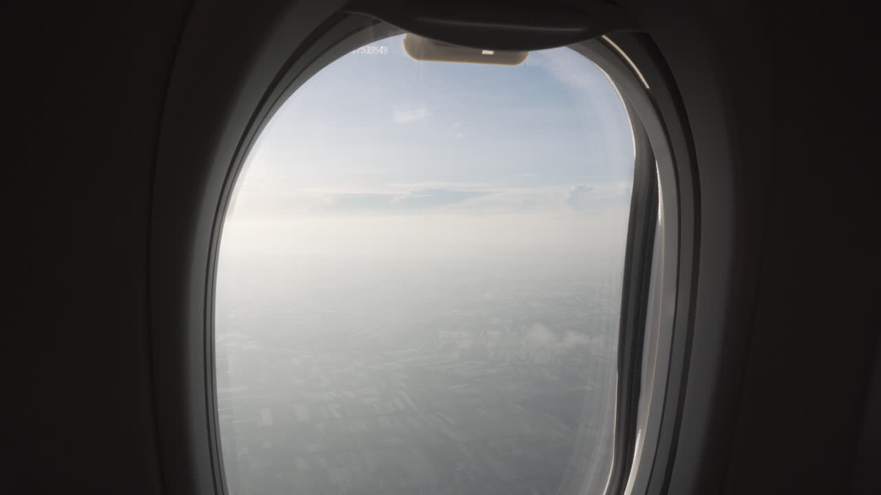 4K shot reveal upwards of the view of a flying plane passenger through the window seeing fields and clouds.