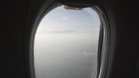 4k shot reveal upwards of the view of a flying plane passenger through the window seeing fields and clouds.