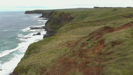 fast moving aerial shot moving over green fields on the edge of where the land meets the sea with big cliffs