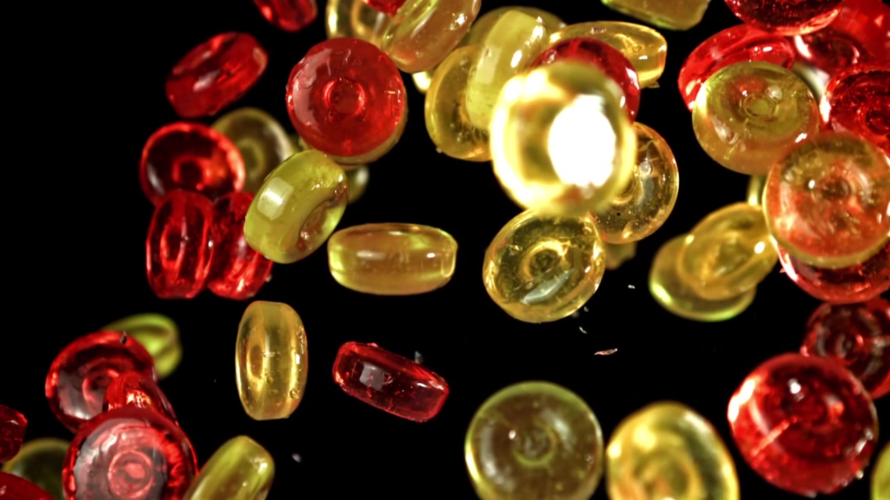 Caramelle rosse e gialle che cadono al rallentatore su sfondo nero