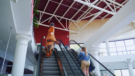 person in a t-rex costume on an escalator in a shopping mall