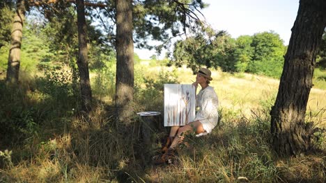 artist forcefully painting on a large canvas in a serene field a craftsperson wearing a black hat checkered shirt and jeans is energetically painting a large canvas in the middle of a peaceful grass field