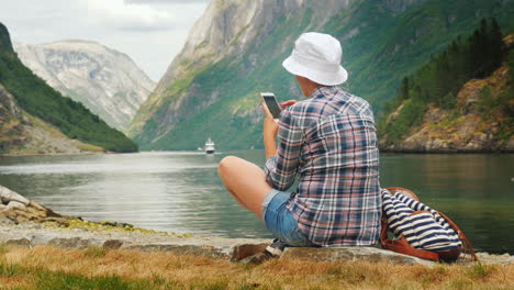 una mujer usa un teléfono inteligente en la orilla de un pintoresco fiordo en noruega tecnología siempre en contacto o